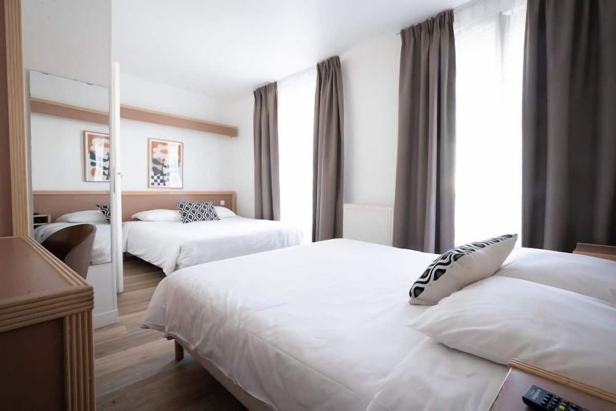 A hotel room with two beds, a wooden dresser, and a mirror.