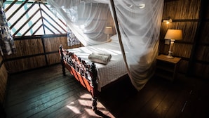Una cama con dosel, suelo de madera, una mesita de noche con lámpara y una ventana con vistas geométricas.