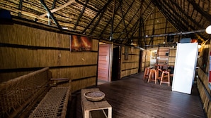 Un interior rústico con un banco tejido, un taburete pequeño y una zona de comedor de madera con taburetes y una mesa.