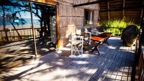 Una terraza de madera con mesa y sillas, una parrilla y vista al océano.