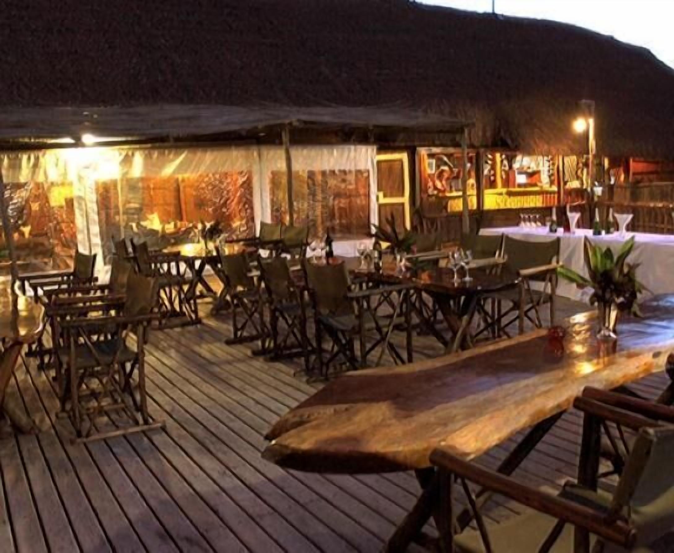 Un espace de restauration en plein air avec des tables et des chaises en bois, un toit de chaume et une vue sur le paysage environnant.