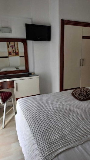 Hotellihuone, jossa on sänky, työpöytä, tuoli, vaatekaappi ja seinälle asennettu televisio.