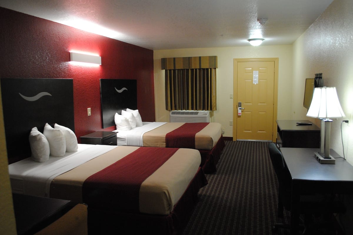 A hotel room with two beds, a desk, a chair, a lamp, and a door.
