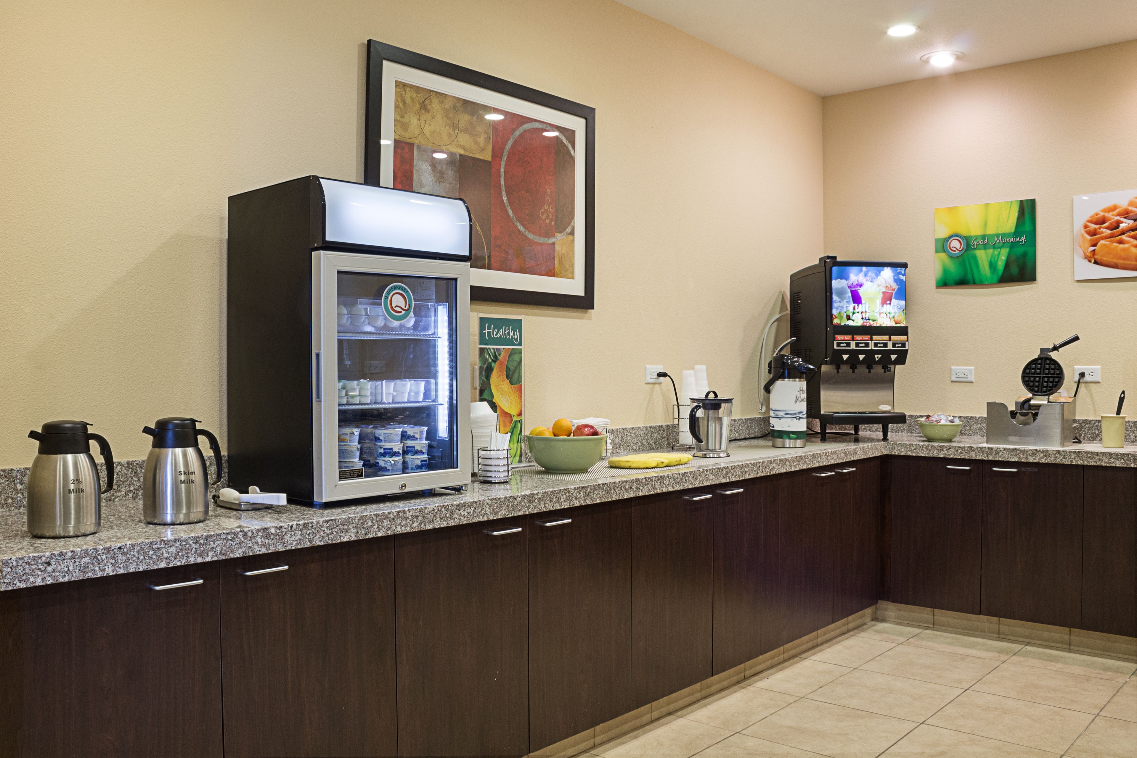 Cozinha equipada com cafeteira, geladeira, micro-ondas, tigela de frutas e máquina de café.
