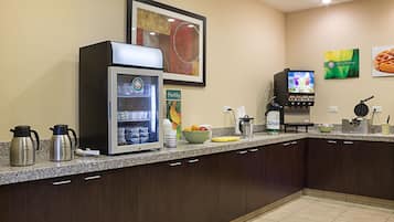 Cozinha equipada com cafeteira, geladeira, micro-ondas, tigela de frutas e máquina de café.