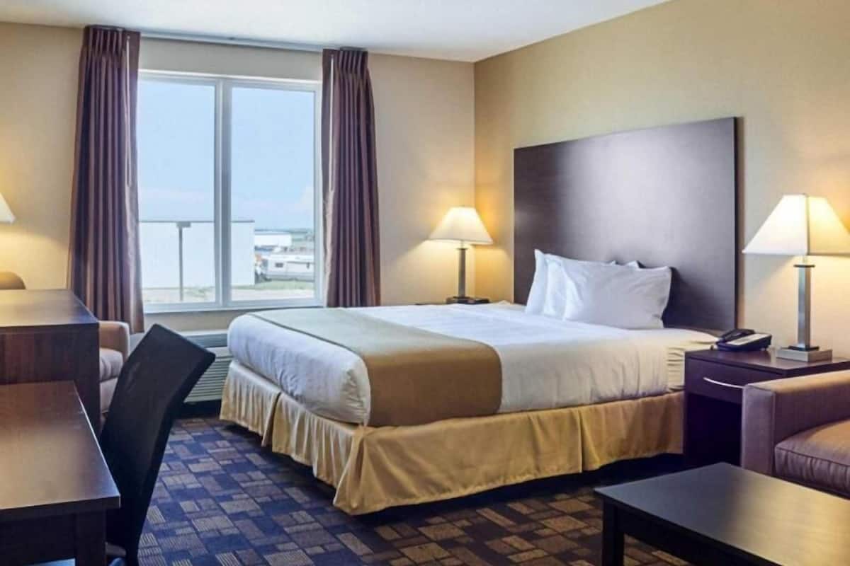 A hotel room with a large bed, two bedside tables with lamps, a chair, a desk, and a view of the outside.