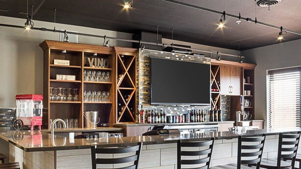 A bar area with a long counter, multiple bar stools, and a variety of bottles and glasses on shelves.