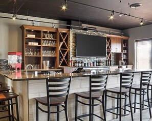 Una zona de bar con una barra larga, varios taburetes y una variedad de botellas y vasos en estanterías.