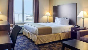 A hotel room with a large bed, two bedside tables with lamps, a desk, a chair, and a view of the outside.