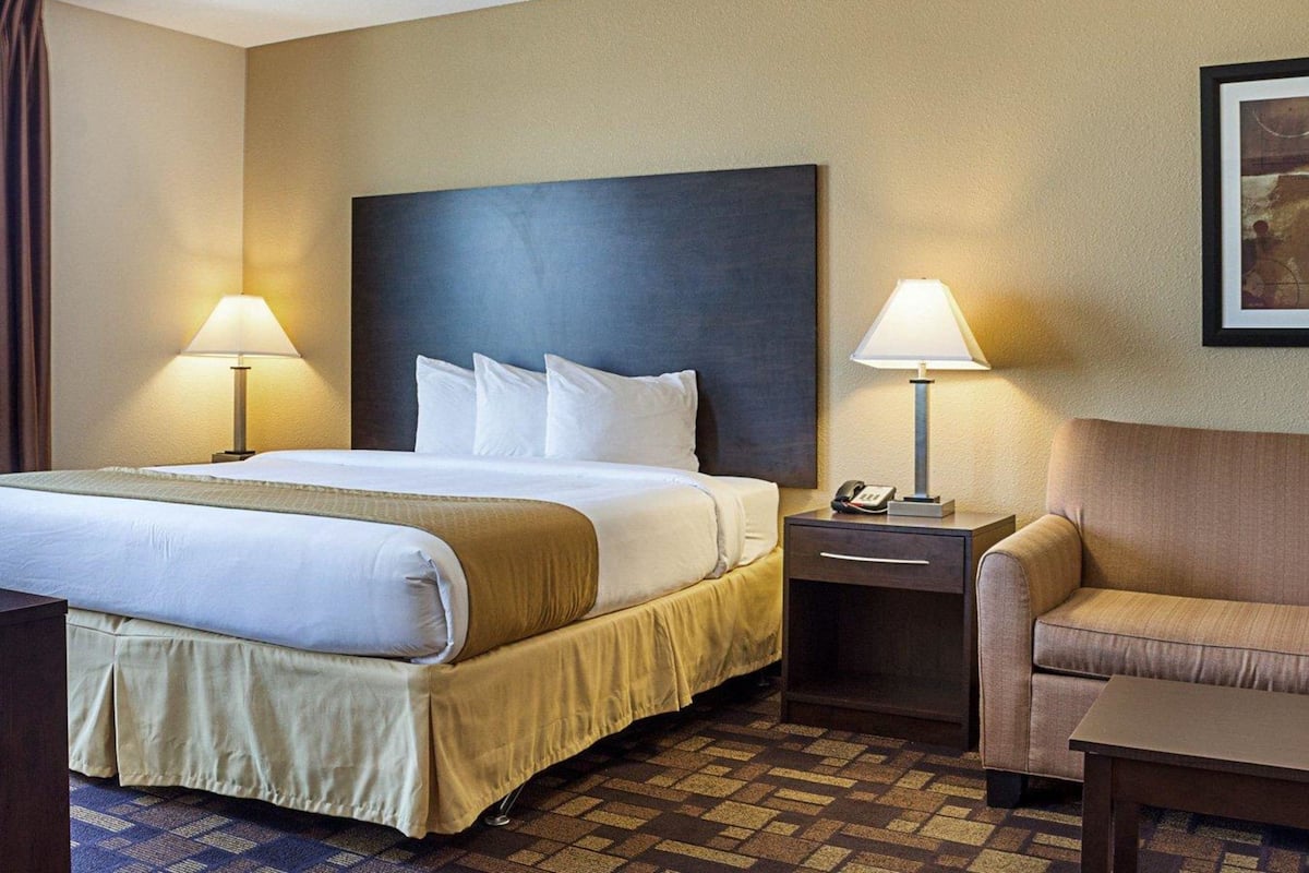A hotel room with a large bed, two bedside tables with lamps, a chair, and a framed picture on the wall.