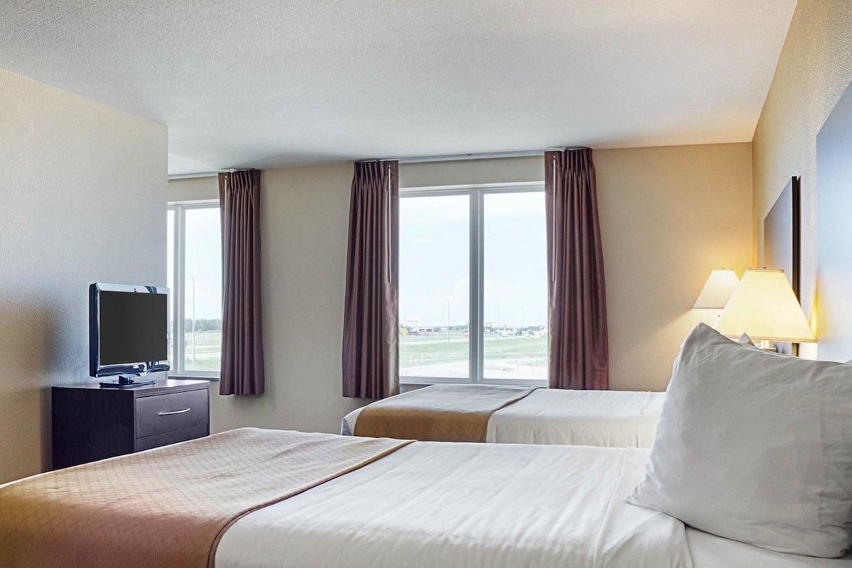 A hotel room with two beds, a TV on a dresser, and a window with curtains.