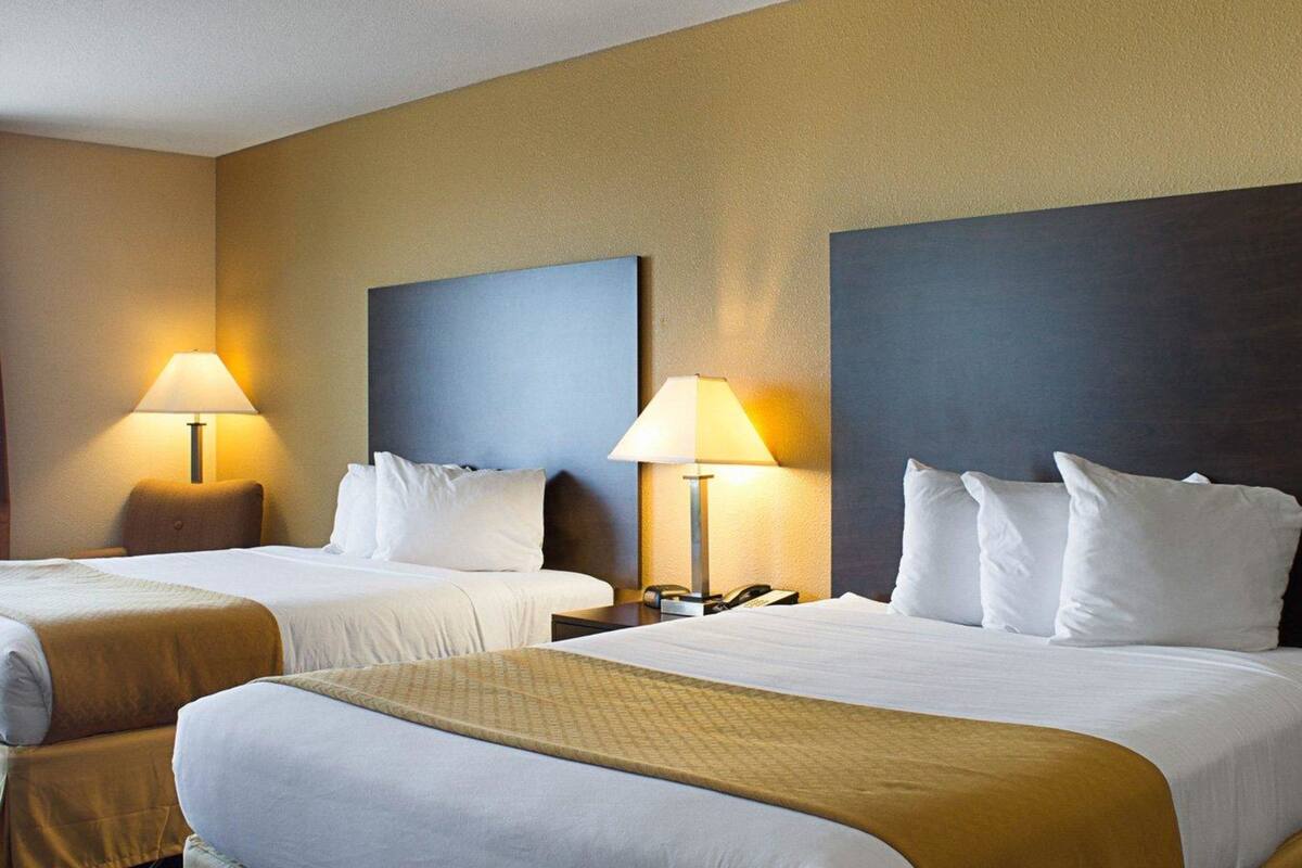 A hotel room with two beds, each with a headboard, bedside lamps, and a neutral color scheme.