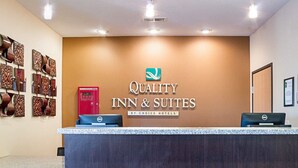 A reception desk at Quality Inn & Suites with a sign, a red phone, and a Dell computer.