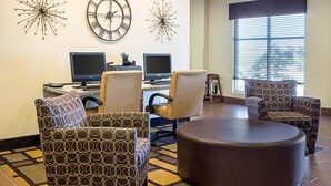 A hotel lobby with two computer desks, three patterned armchairs, a round ottoman, and decorative wall clocks.