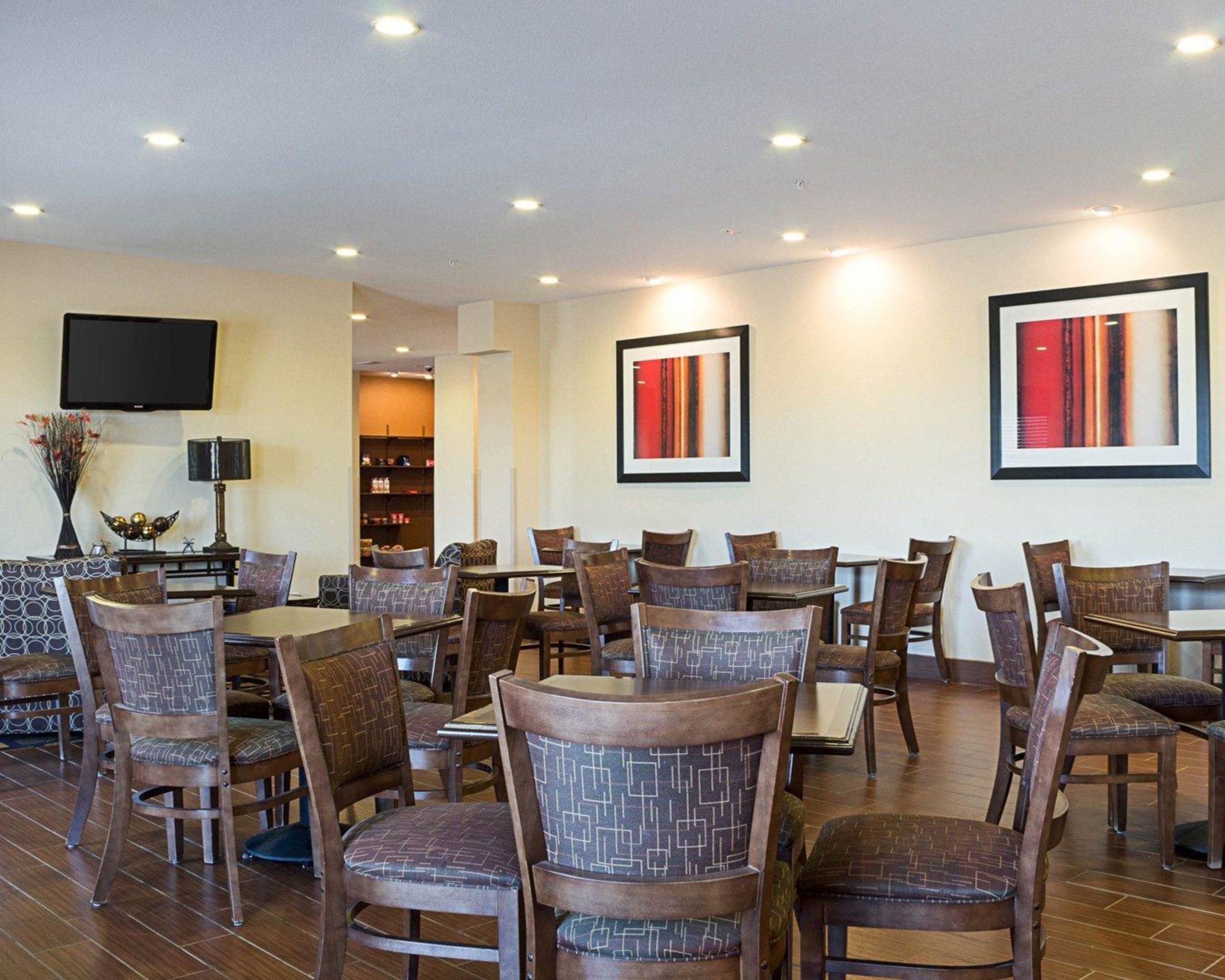 A dining area with multiple tables and chairs, a flat-screen TV mounted on the wall, and framed artwork on the walls.