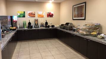 A breakfast bar with various food items and beverages, including waffles, juice, and fruits.