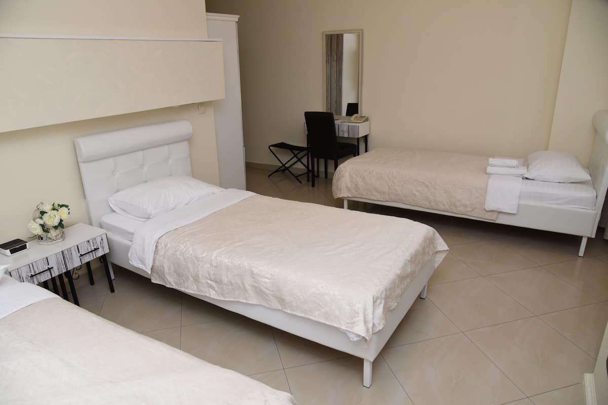 A hotel room with two single beds, a small desk with a chair, a mirror, and a vase with flowers.