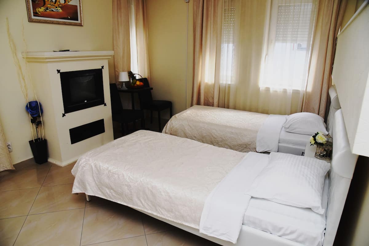 A hotel room with two beds, a desk, a chair, a TV, and a fireplace.