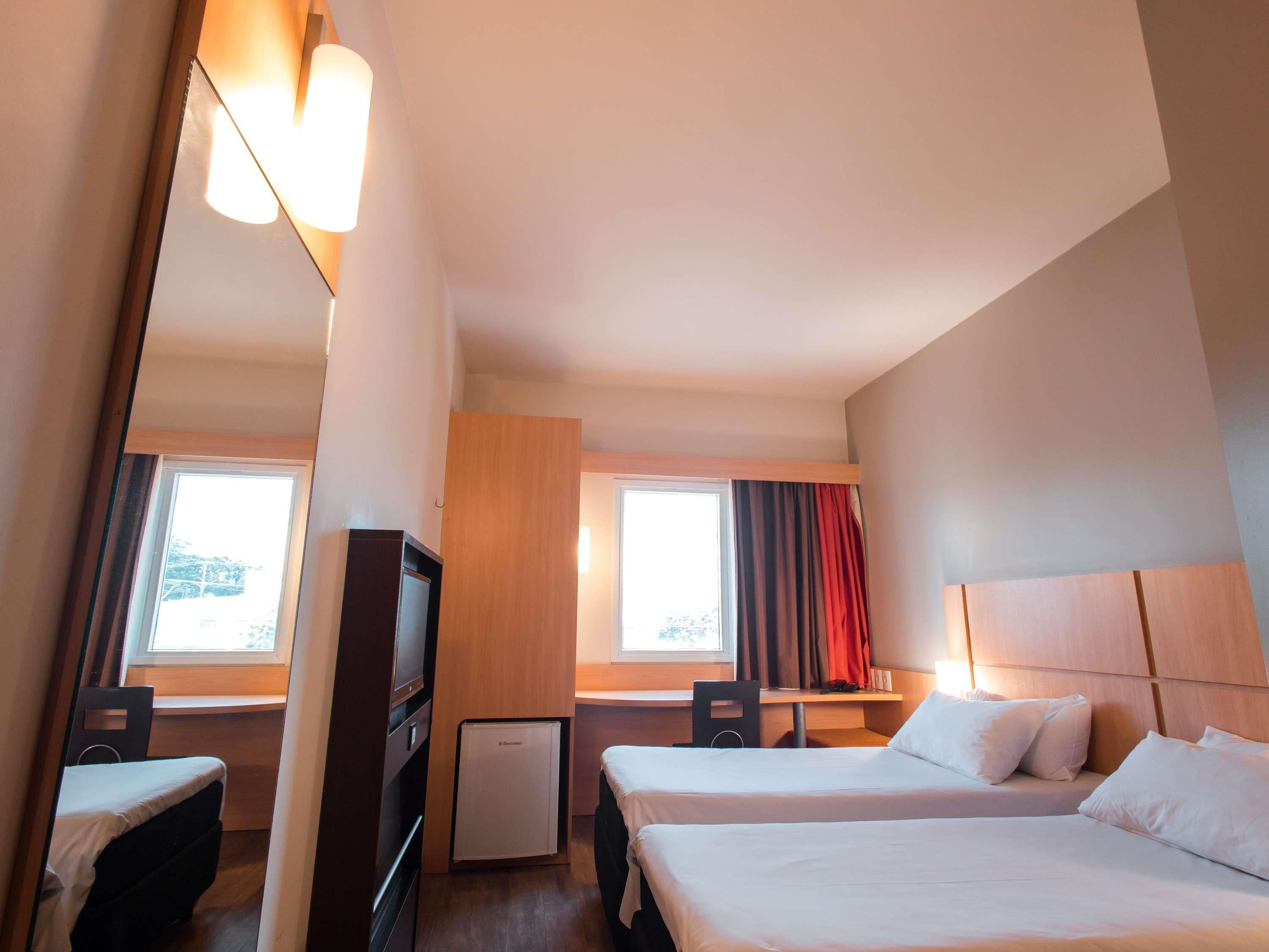 A hotel room with two beds, a desk, a chair, a television, and a minibar.