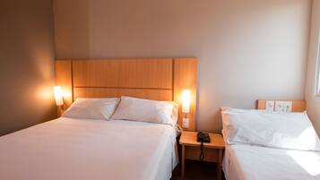 A hotel room with two beds, each with a wooden headboard and bedside lamps. There is a nightstand with a phone and a power outlet between the beds.