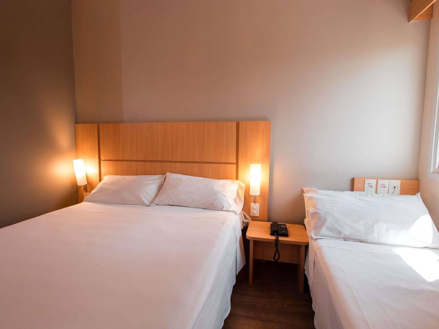 A hotel room with two beds, each with a wooden headboard and bedside lamps. There is a nightstand with a phone and a power outlet between the beds.