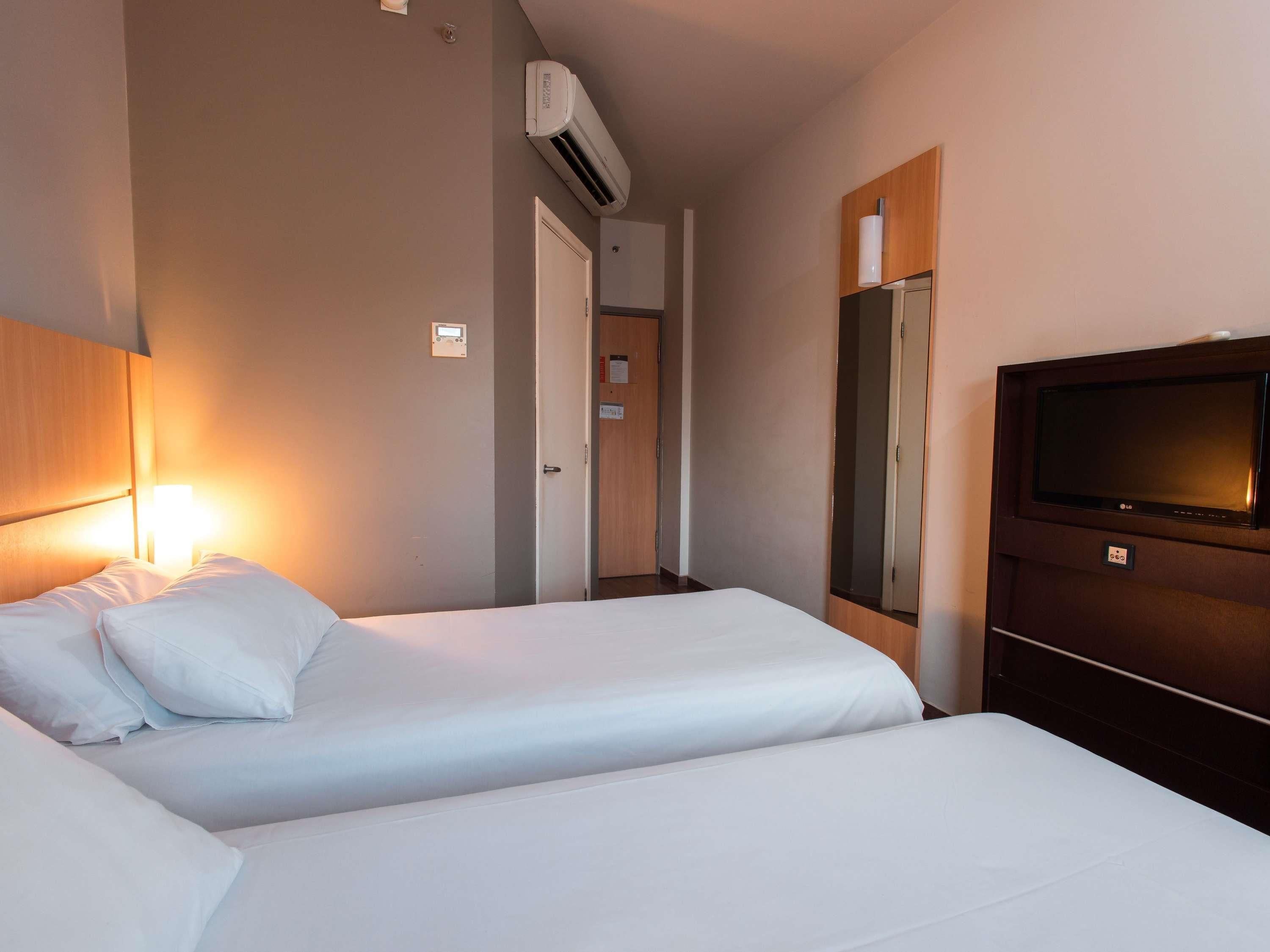 Hotellihuone, jossa on kaksi sänkyä, televisio, ilmastointilaite ja puinen pääty.