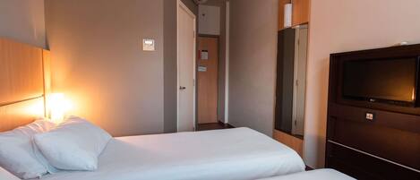 Hotellihuone, jossa on kaksi sänkyä, televisio, ilmastointilaite ja puinen pääty.