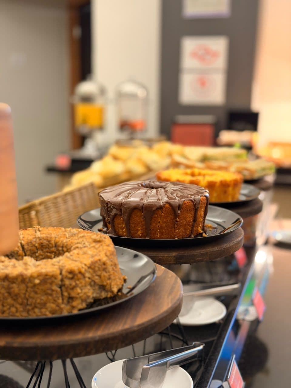 A buffet table with various baked goods, including a chocolate-glazed cake and a fruit-topped cake.