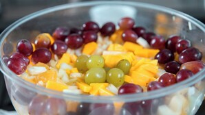 A clear glass bowl containing a fruit salad with grapes, mango chunks, and other fruits. - ibis Presidente Prudente Manoel Goulart (Presidente Prudente)