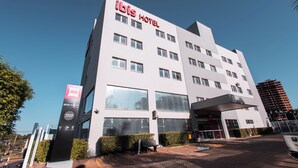 A modern hotel building with a prominent "ibis Hotel" sign, large windows, and a covered entrance.
