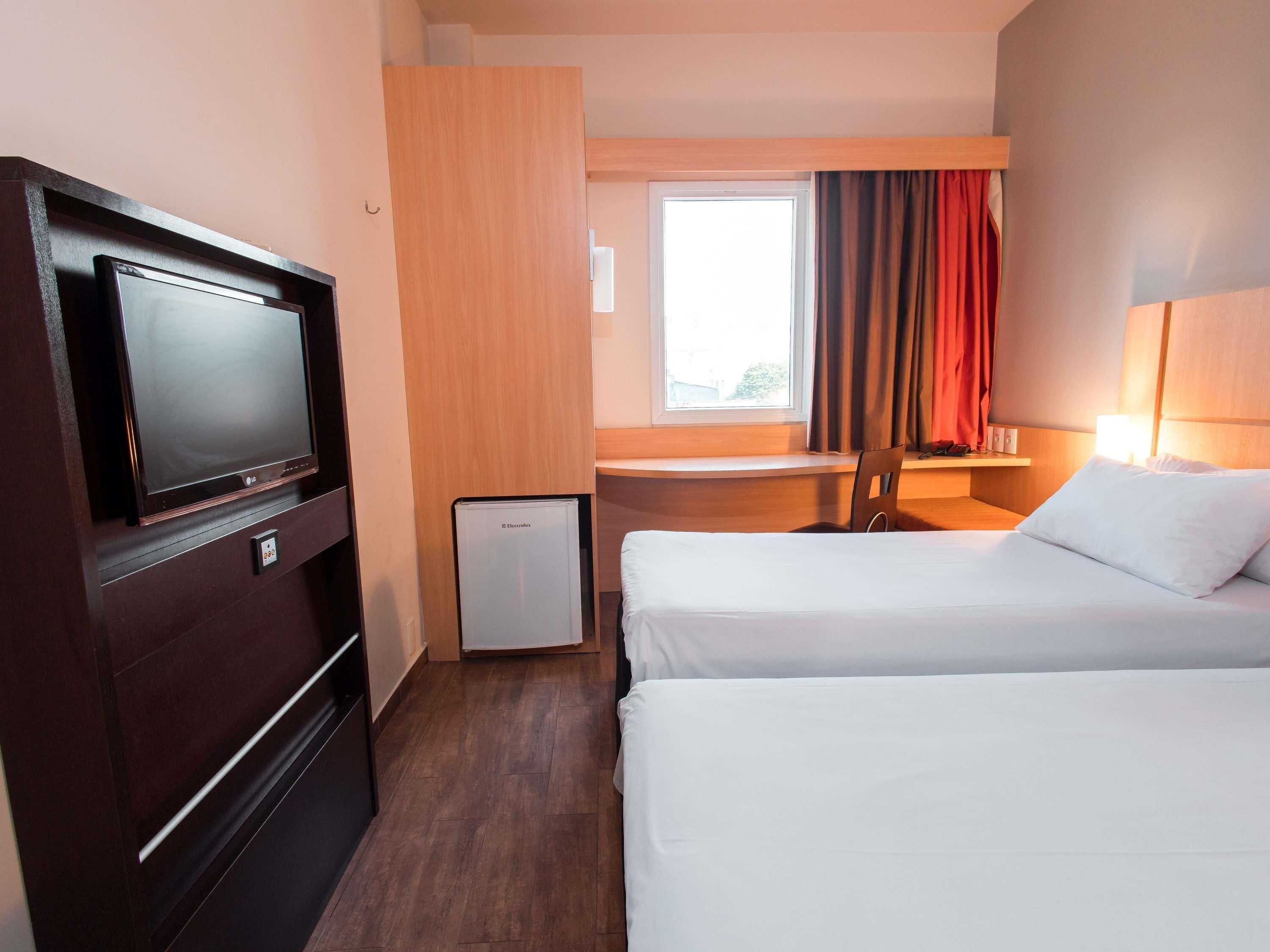 Habitación de hotel con cama, escritorio, silla, televisión y refrigerador pequeño.