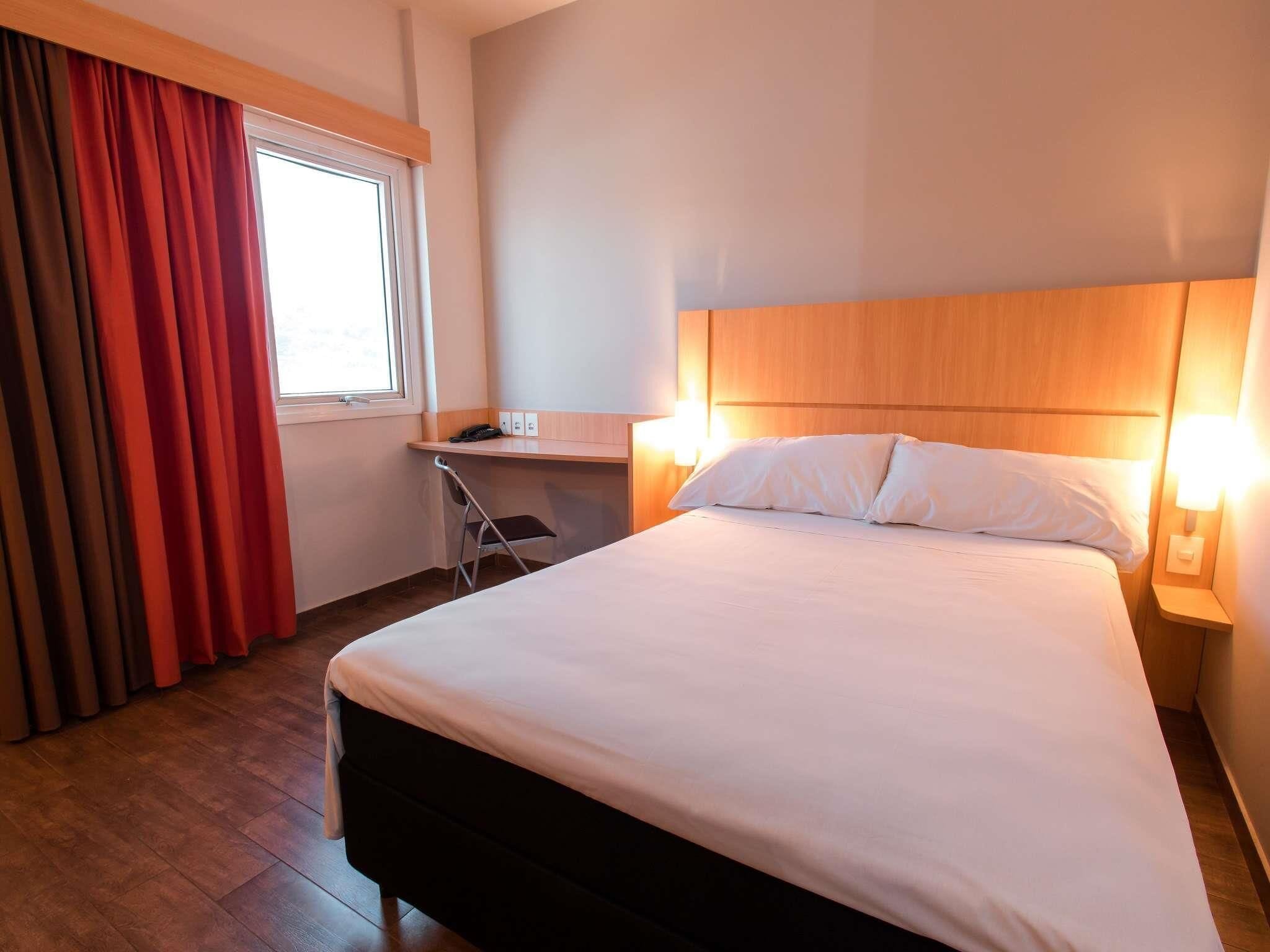 Hotellihuone, jossa on sänky, työpöytä, tuoli ja ikkuna, jossa on verhot.
