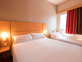 Quarto de hotel com uma cama grande, duas mesas de cabeceira, uma janela com cortinas e uma cabeceira de madeira.
