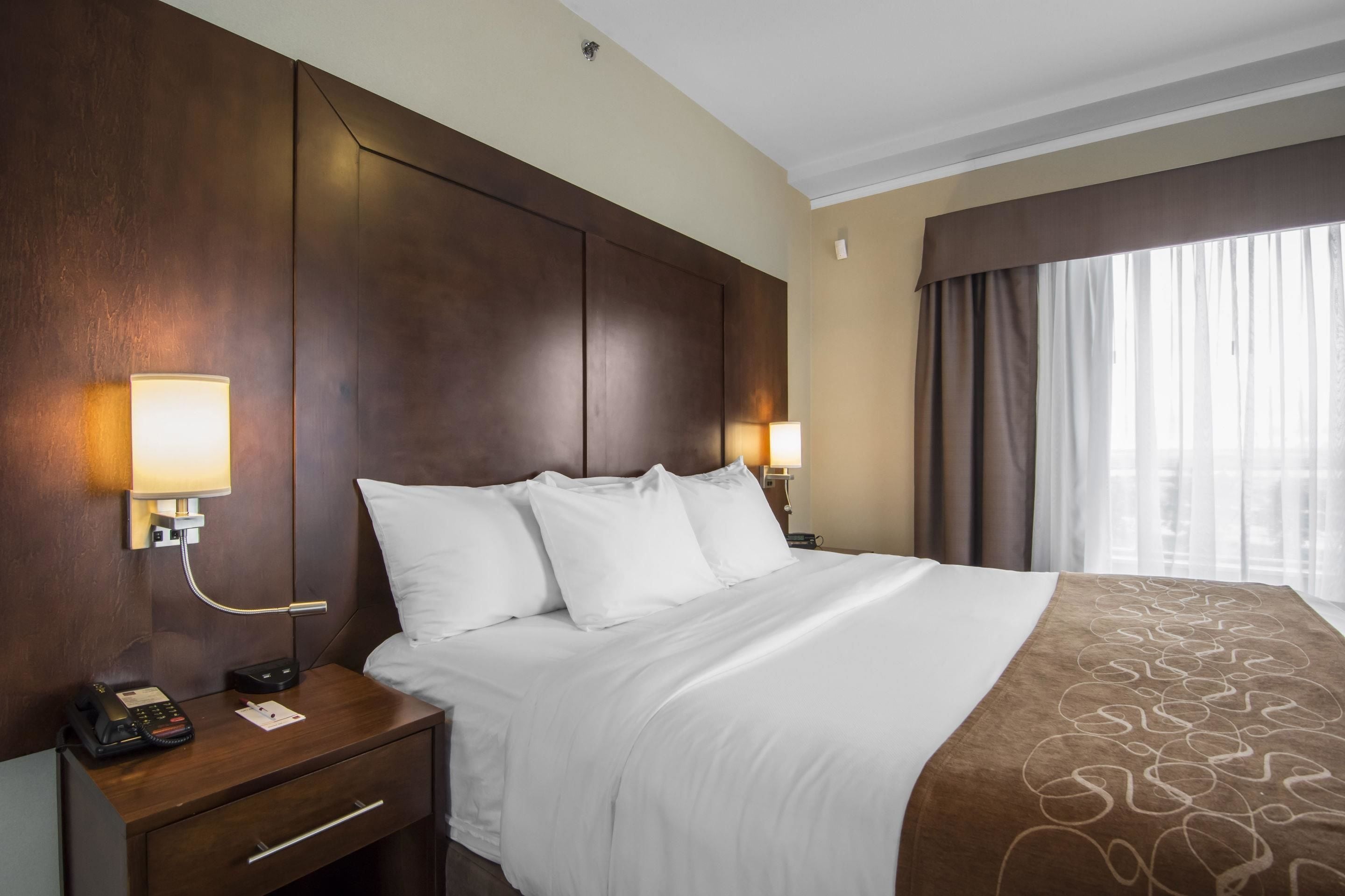 A hotel room with a large bed, two bedside lamps, a nightstand with a phone, and a window with curtains.