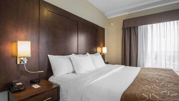A hotel room with a large bed, two bedside lamps, a nightstand with a phone, and a window with curtains.
