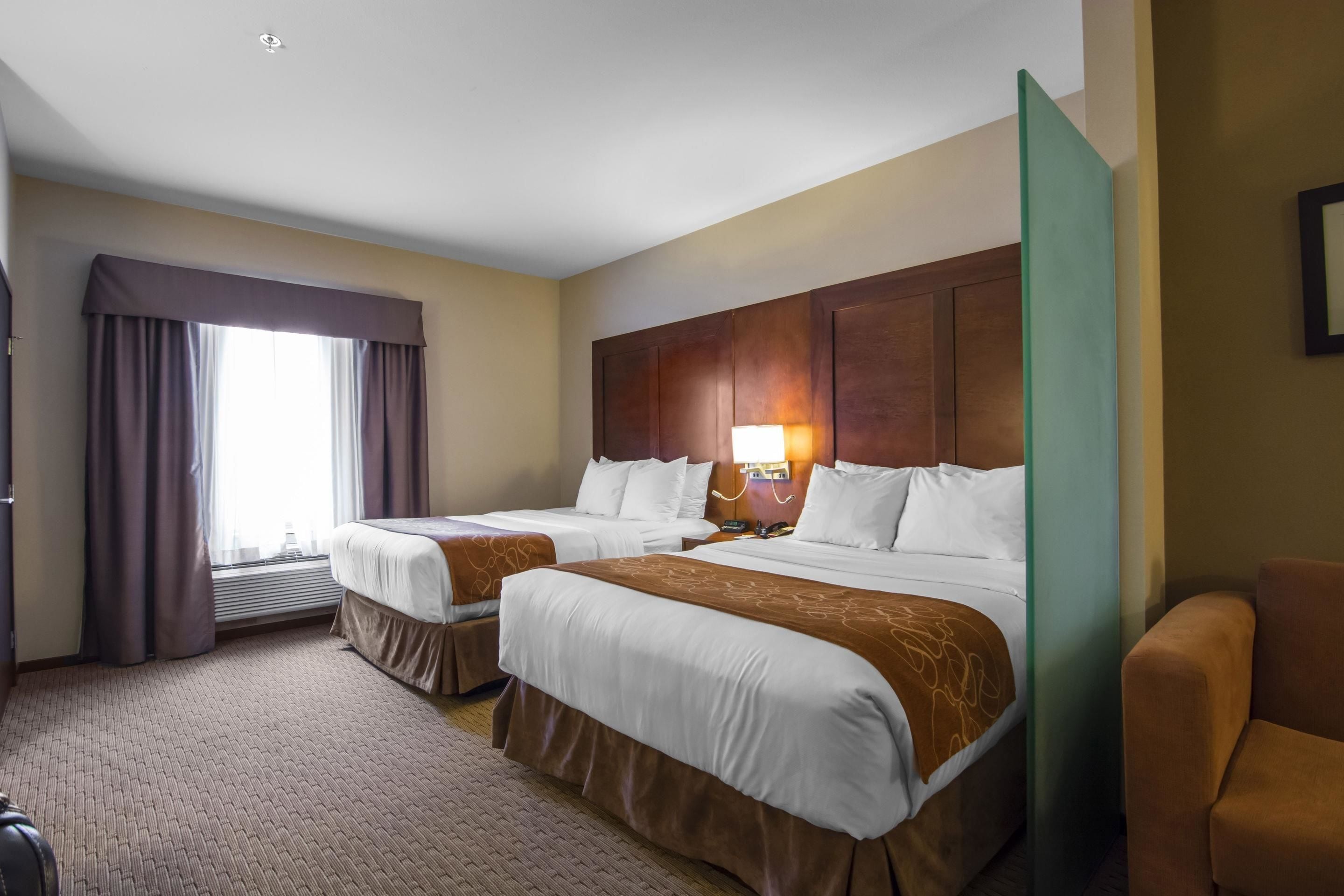 Een hotelkamer met twee bedden, een groot raam met gordijnen, een wandlamp en een groen scheidingswand.