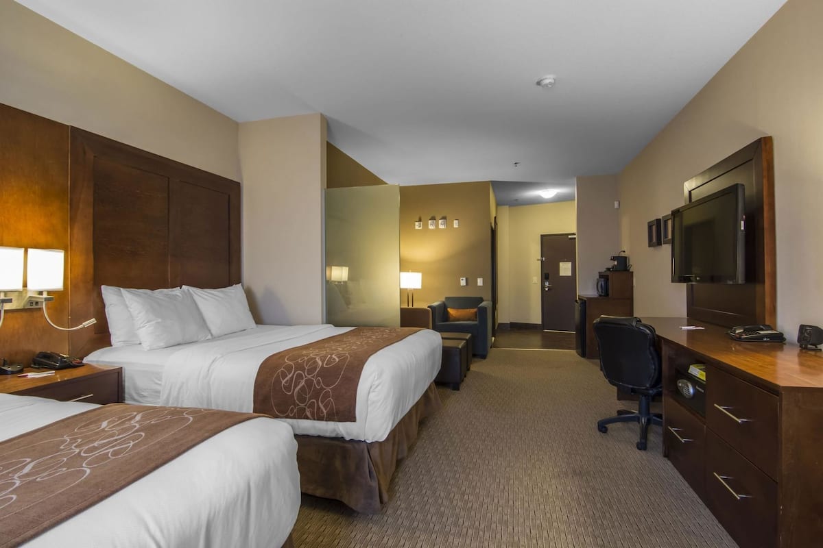A hotel room with two beds, a desk, a chair, a TV, and a minibar.