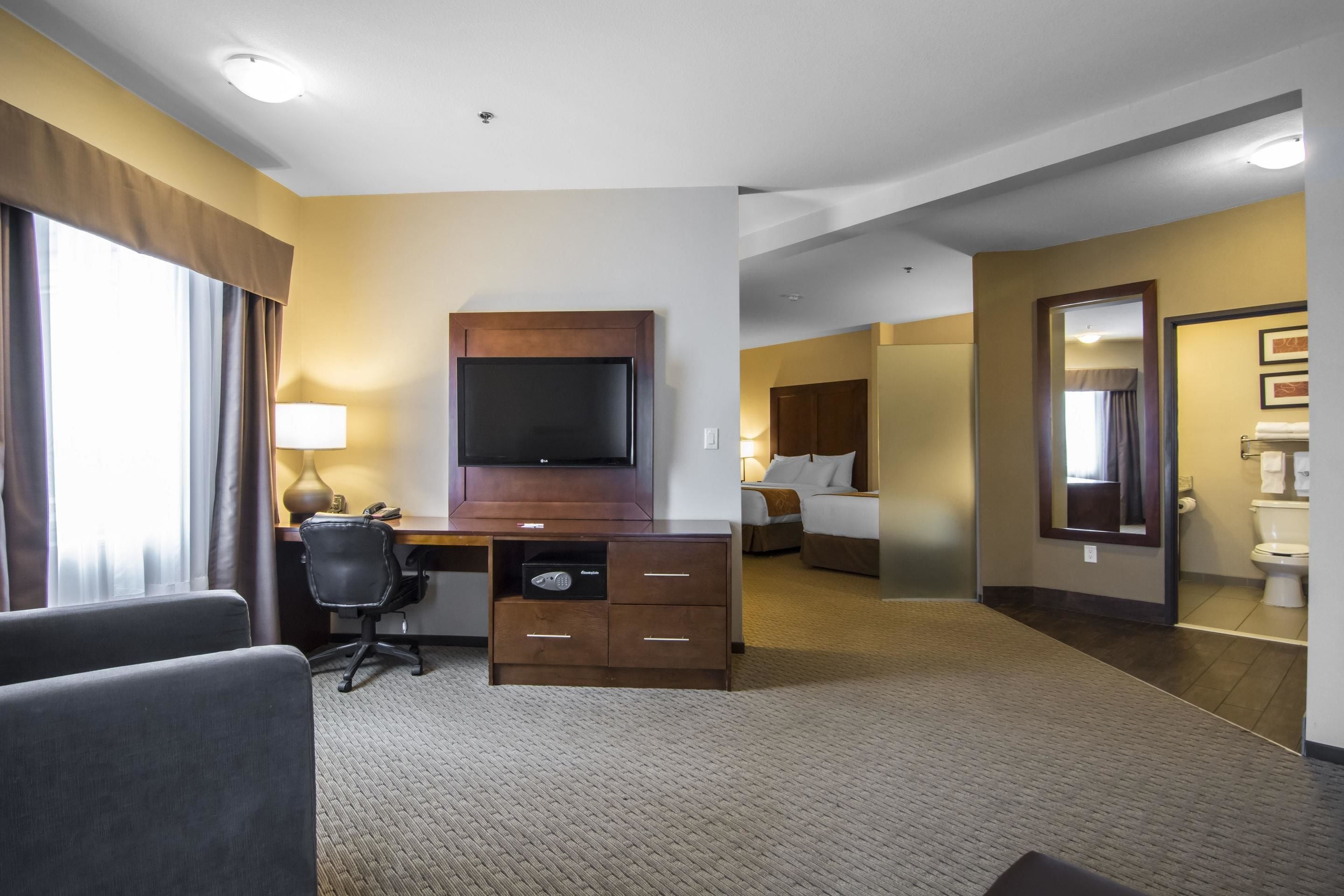 A hotel room with a desk, chair, TV, and a bed.