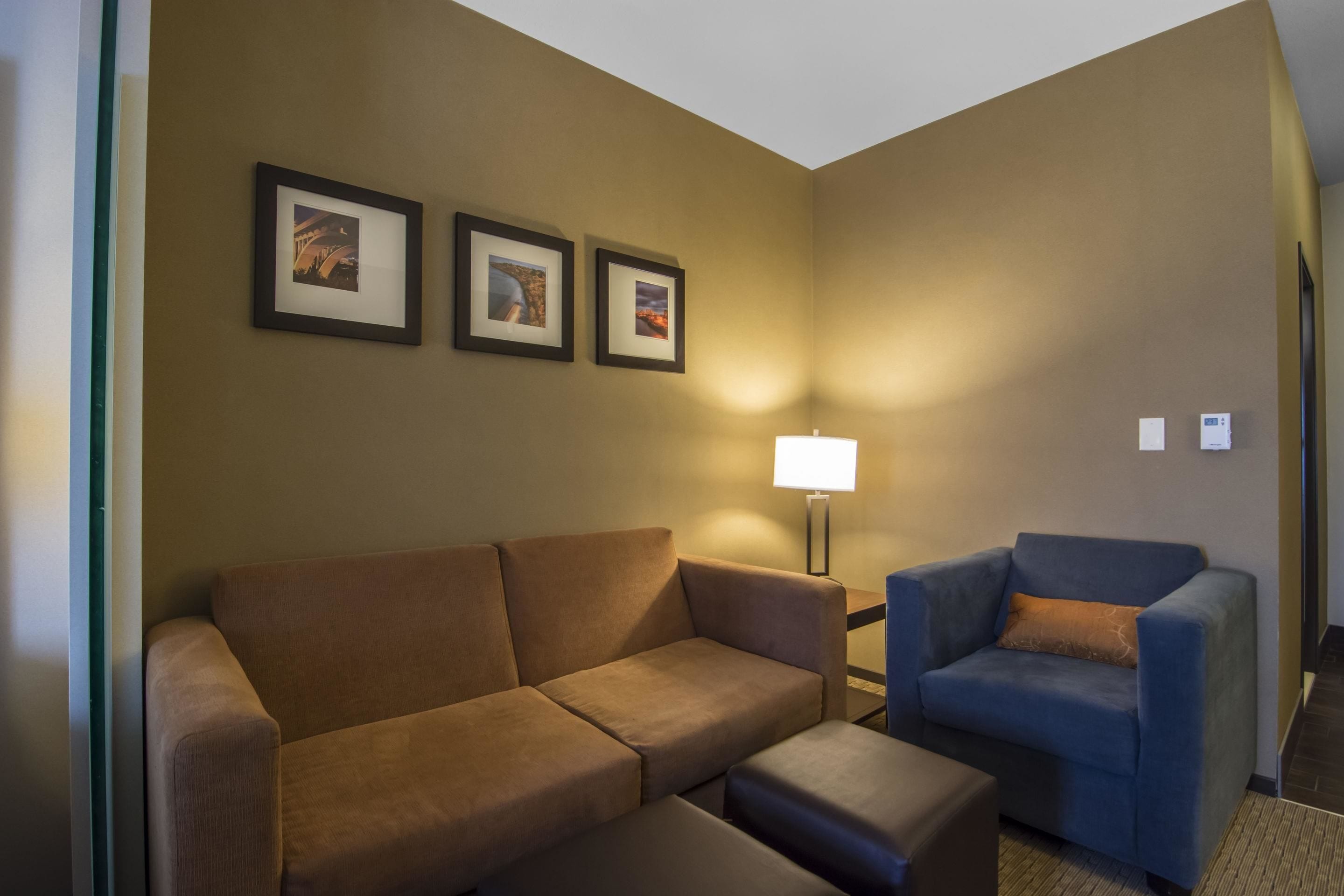 Ein Zimmer mit einem braunen Sofa, einem blauen Sessel und einem kleinen Tisch. An der Wand hängen drei gerahmte Bilder.