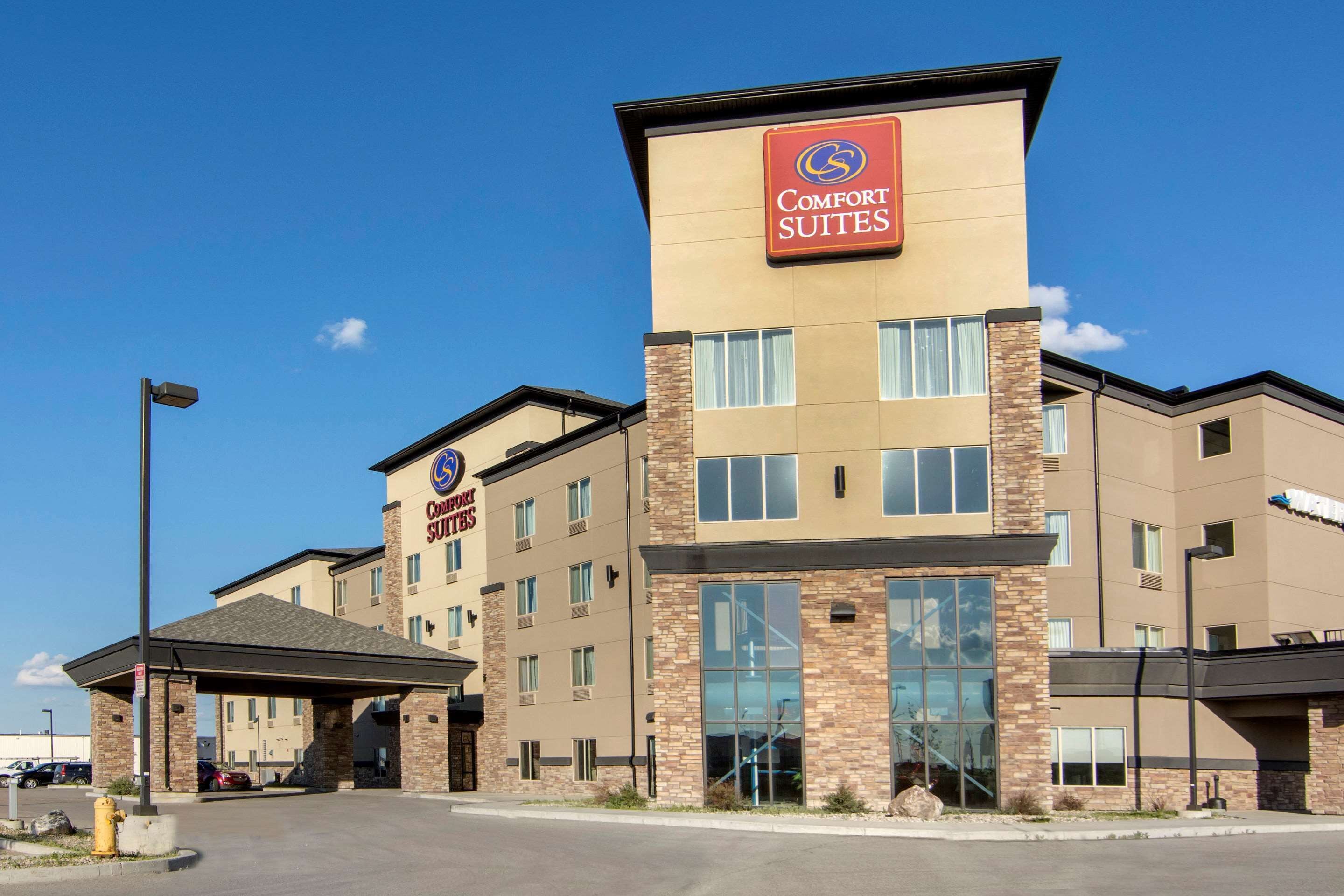 Un hotel Comfort Suites con un diseño moderno, que presenta un letrero llamativo, varios pisos y una zona de estacionamiento cubierta.
