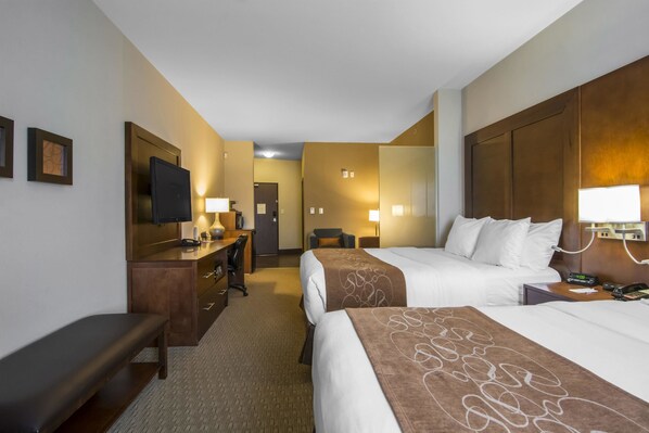 A hotel room with two beds, a desk, a chair, a bench, and a television.