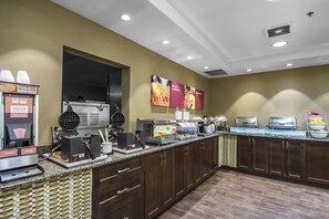 A breakfast bar with waffle makers, coffee machines, and a fruit bowl.