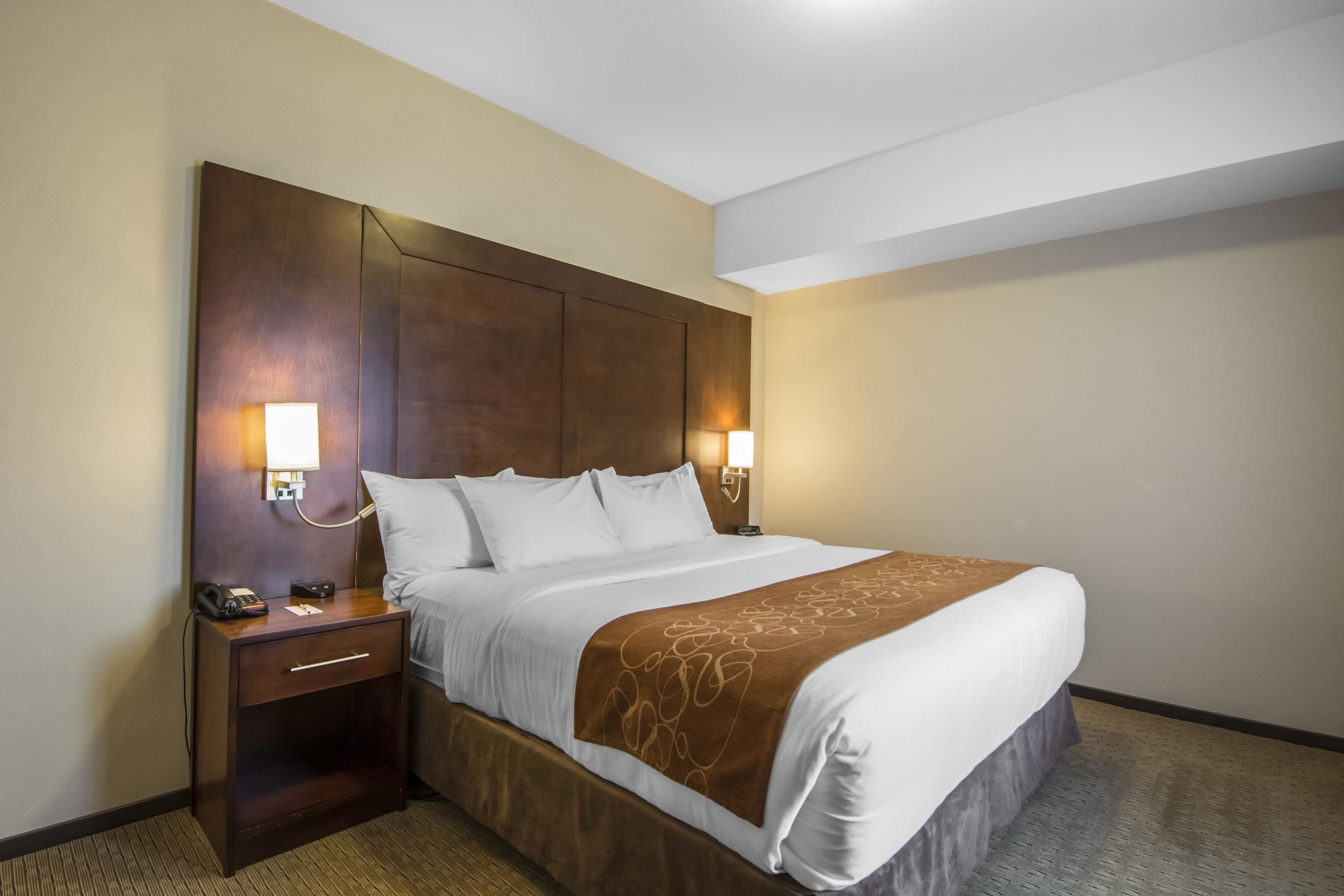 Quarto de hotel com uma cama grande, duas luminárias de cabeceira, mesa de cabeceira com telefone e cabeceira marrom.