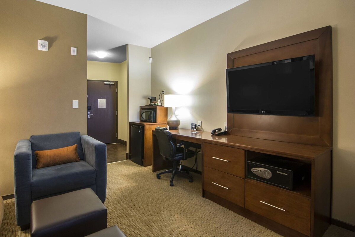 A hotel room with a desk, chair, television, microwave, and a small refrigerator.