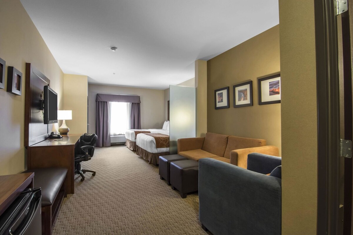 A hotel room with a bed, two sofas, a desk with a chair, a television, and a window with curtains.
