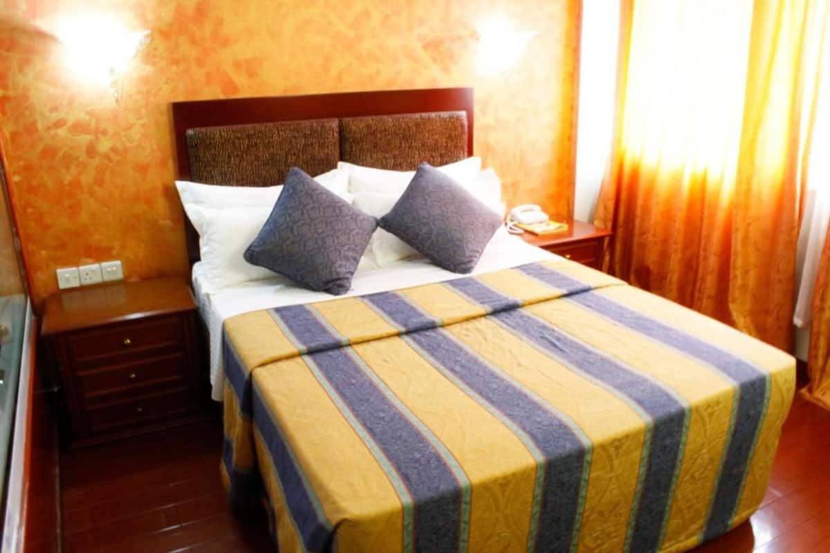 A hotel room with a wooden headboard, a striped bedspread, a nightstand, and a telephone.