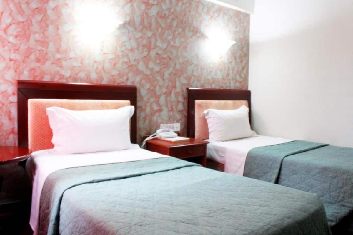 A hotel room with two single beds, a nightstand with a phone, and a wall with a floral pattern.