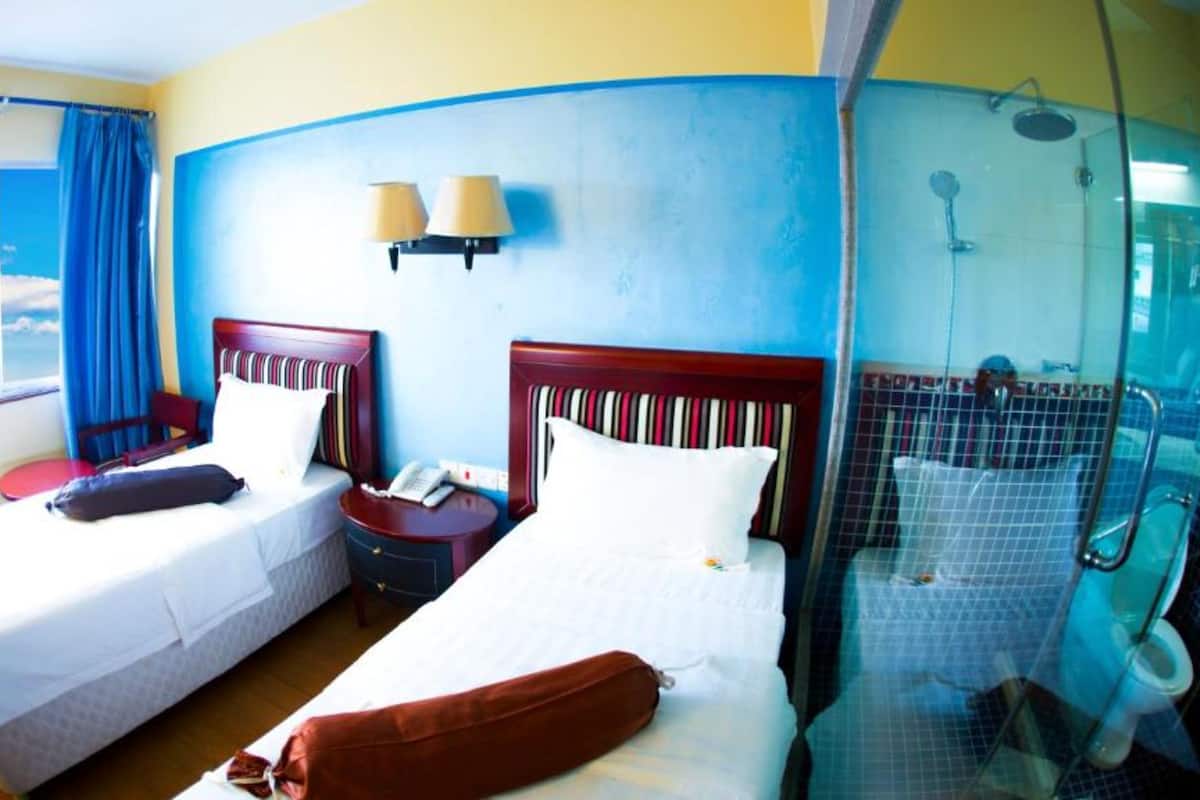 A hotel room with two beds, a shower, and a window with curtains.