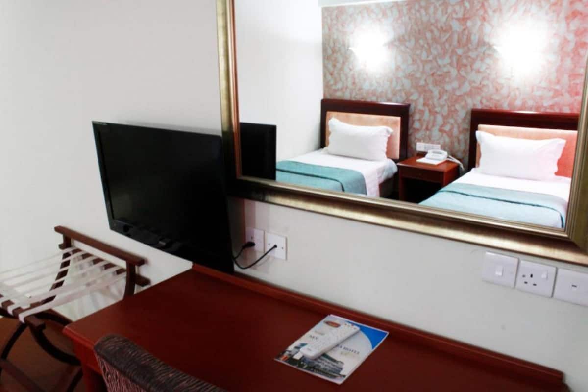 A hotel room with a bed, a TV, a desk, and a mirror.