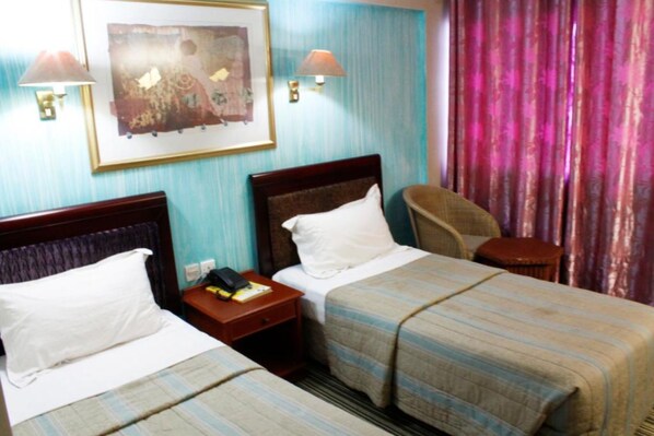 Habitación de hotel con dos camas, una mesita de noche, una silla y un cuadro en la pared.